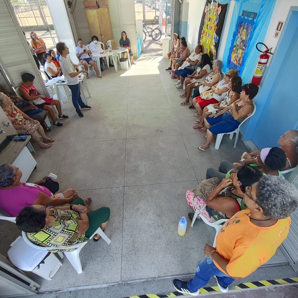 Foto com pessoas idosas frequentadoras do Centro de Convivência da Terceira Idade, sentadas em roda e ouvindo a fala do psicólogo sobre Prevenção Combinada.